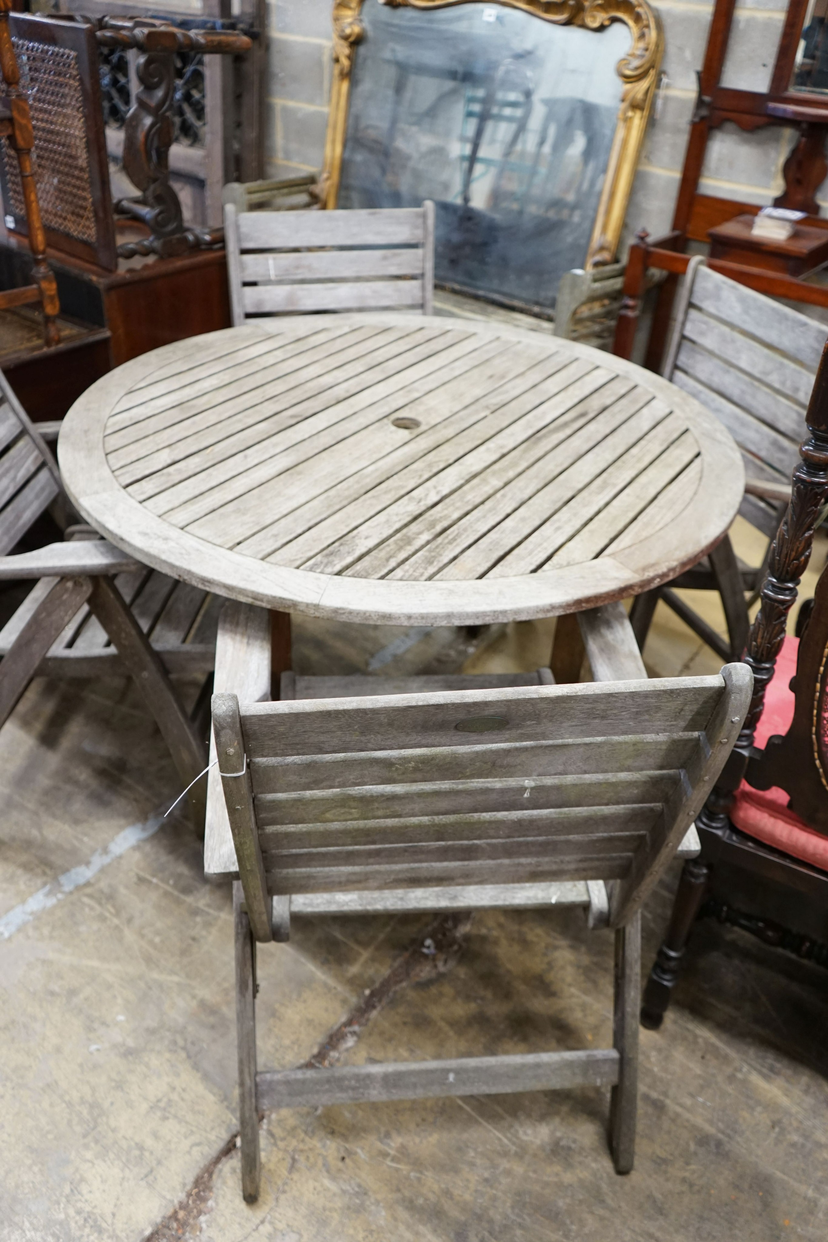 A circular weathered teak slatted garden table, diameter 122cm, height 74cm together with four weathered teak folding garden armchairs